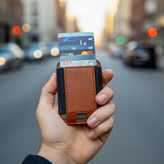 A brown leather MagSafe wallet holding credit cards, attached to the back of an iPhone.