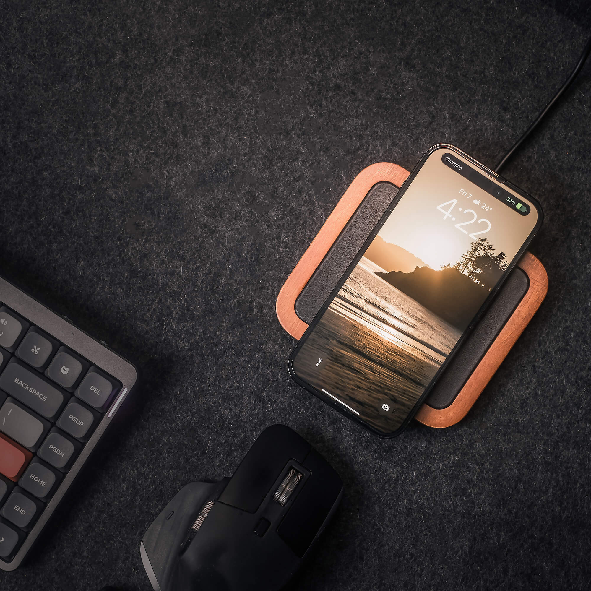 A smartphone showing 4:22 is wirelessly charging on the UNO Black - Single-Coil MagSafe Oak Wireless Charger, beside a computer mouse and part of a keyboard on a dark textured surface.