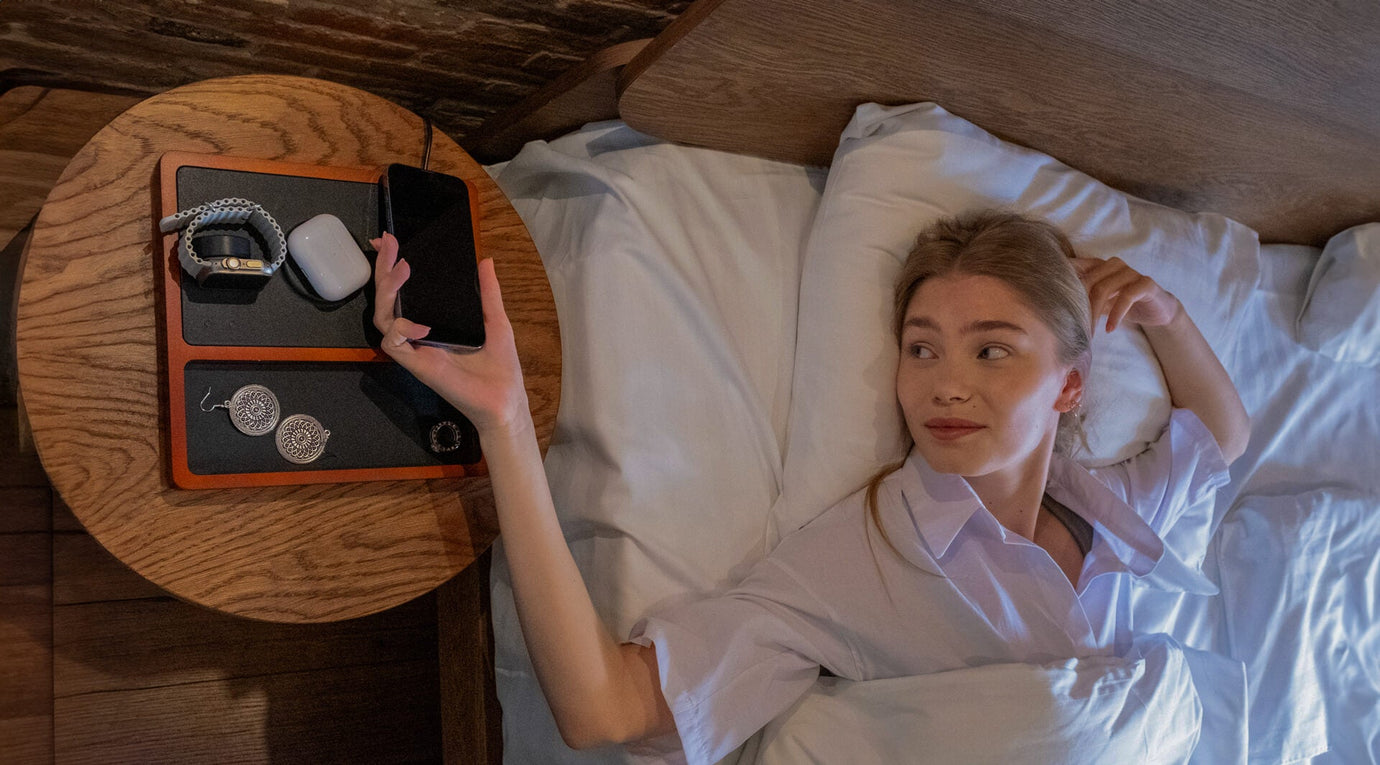 A nightstand organizer with a charging station holding phones, glasses, and notebooks.
