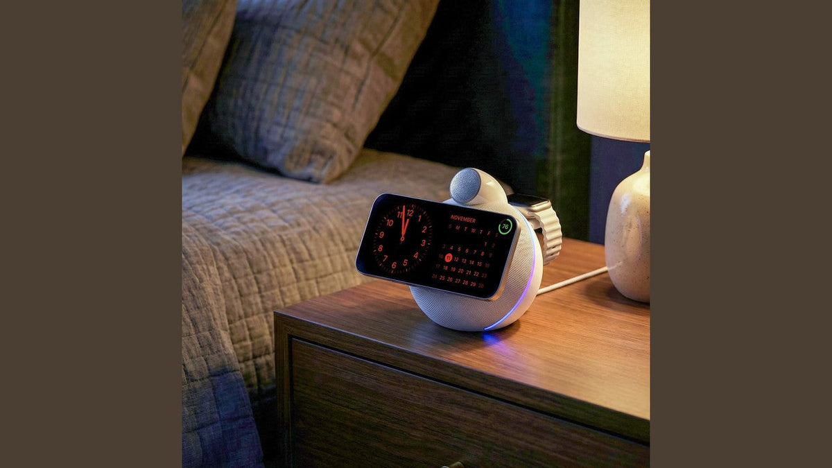 Bedside wireless charging speaker with screen and ambient light on a wooden nightstand next to a lamp.