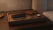 A walnut and leather valet tray charging station holding a phone, wallet, keys, and watch on a nightstand