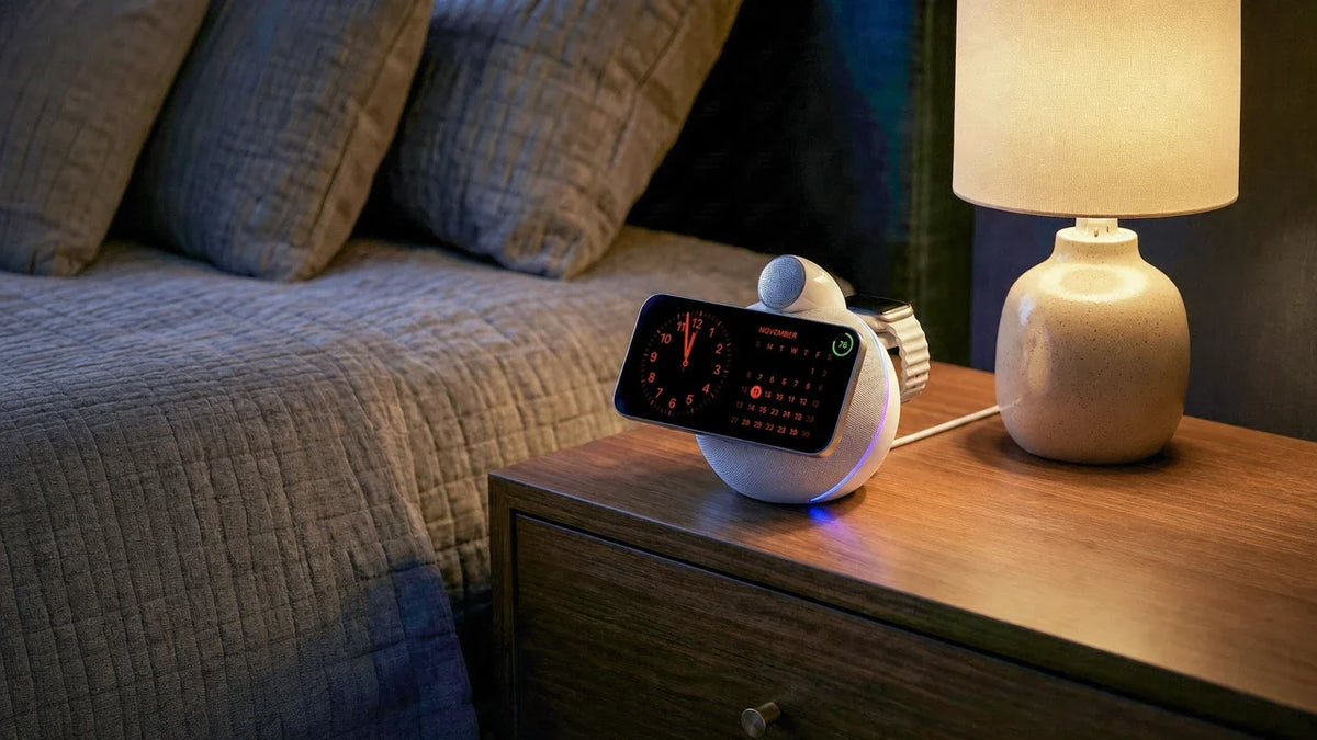 White NYTSTND ORBE Qi2.2 wireless charging speaker on a bedside nightstand, charging an iPhone in StandBy mode and an Apple Watch
