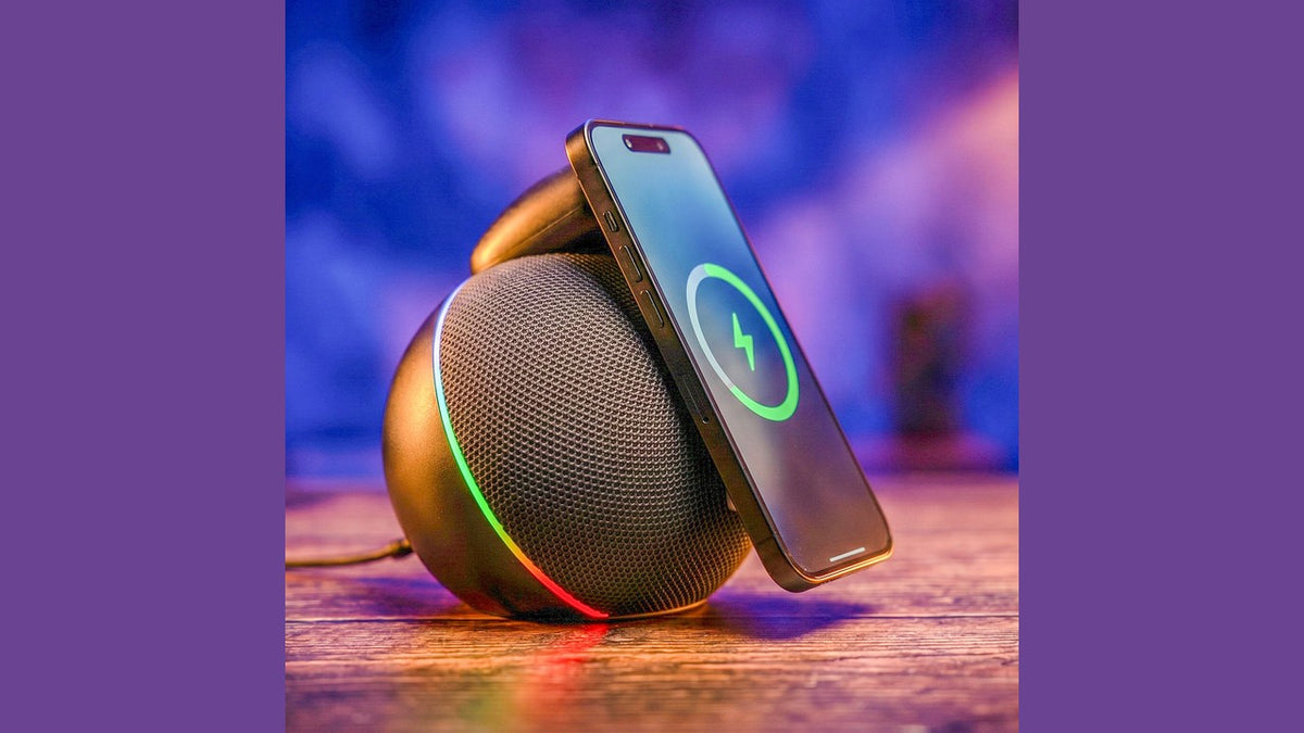 Handcrafted wireless-charging speaker with phone leaning on it, showing charging icon and colored ambient light.